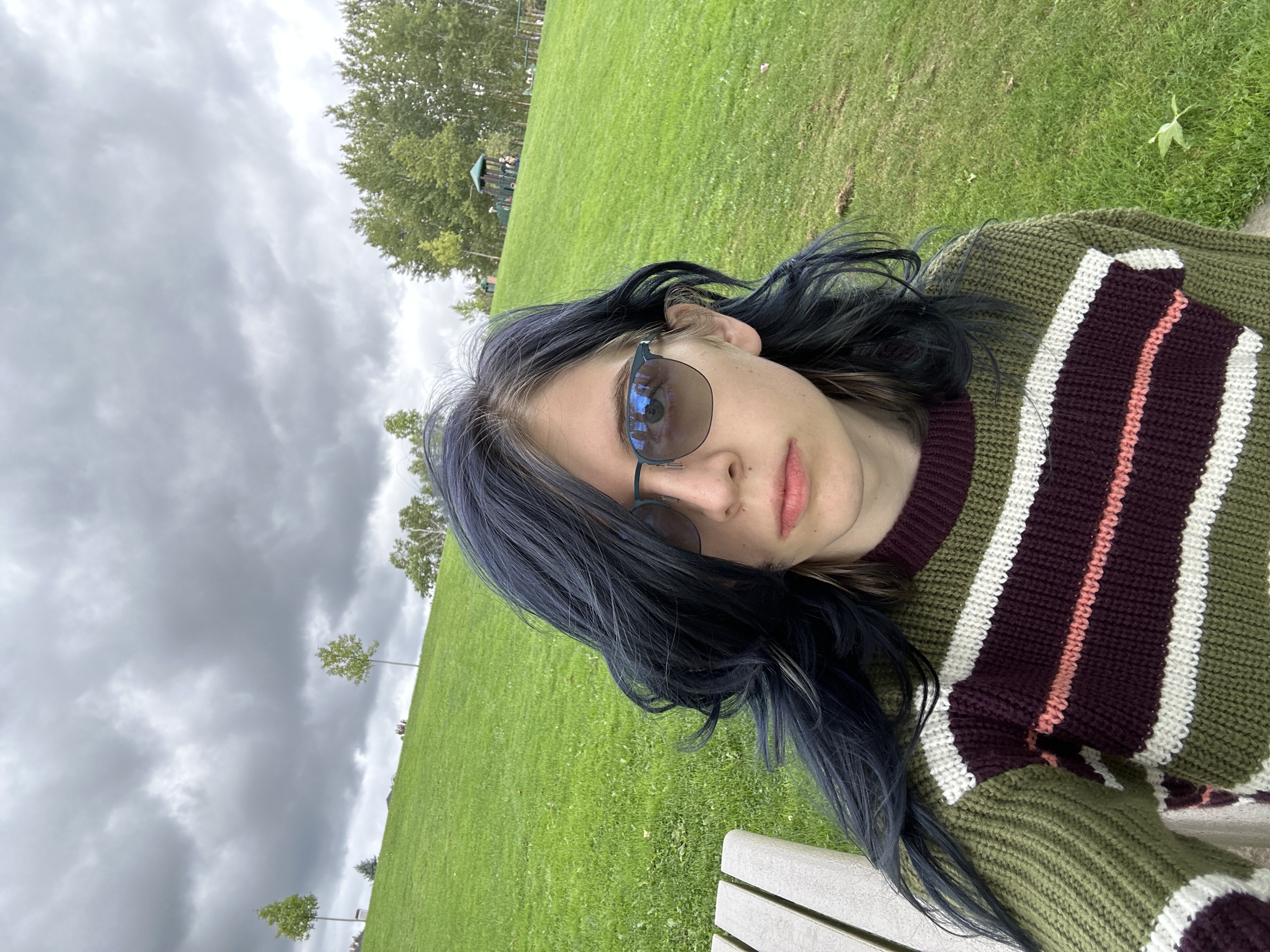 A girl sitting at a park wearing a knit top. I don't wanna alt text this one anymore.